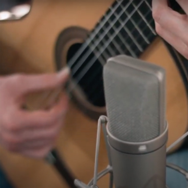 Microfono a condensatore davanti a una chitarra acustica in sala di registrazione